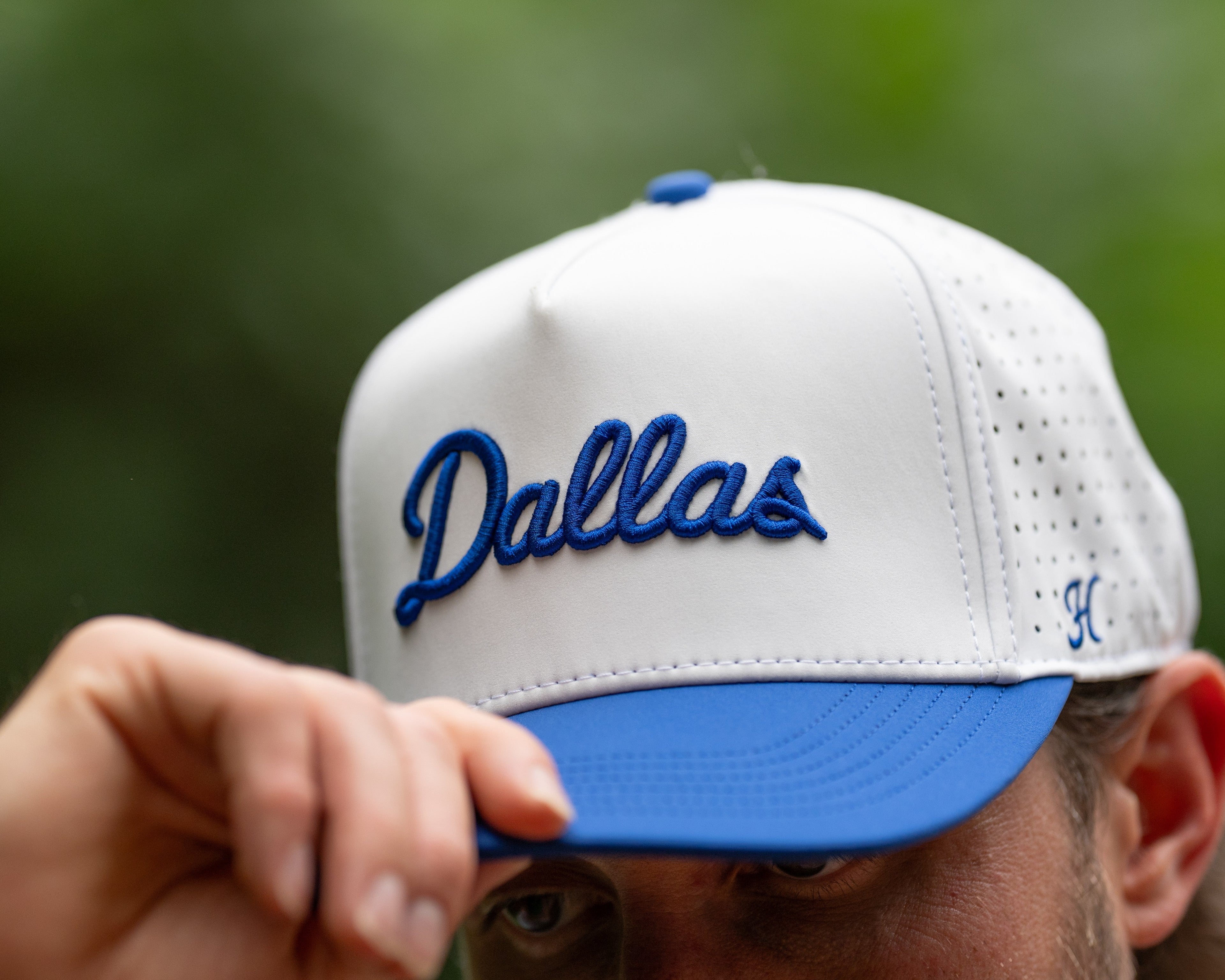 White and blue cap with 'Dallas' text held by a person against a blurred green background