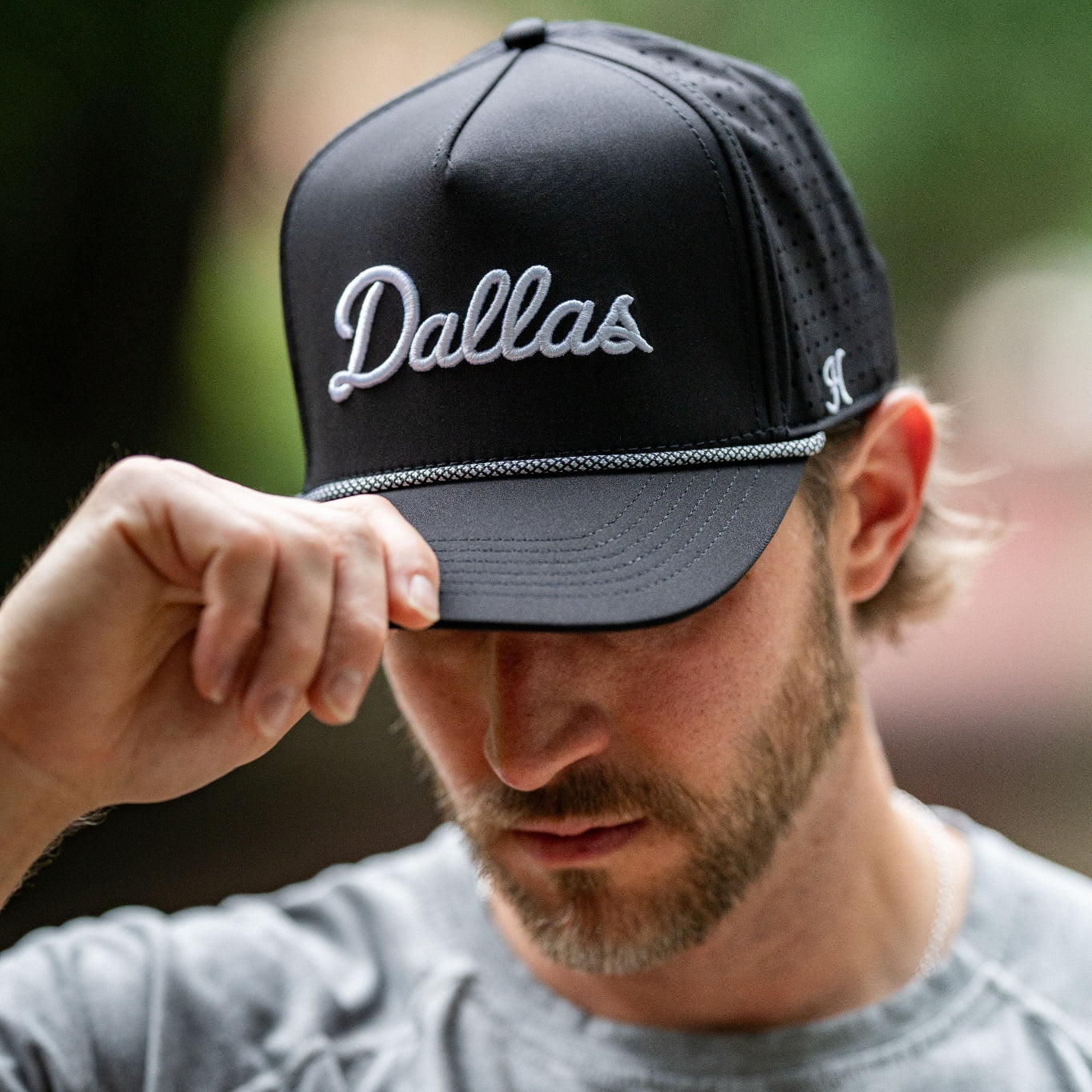 Man wearing a black cap with 'Dallas' printed on it, outdoors.