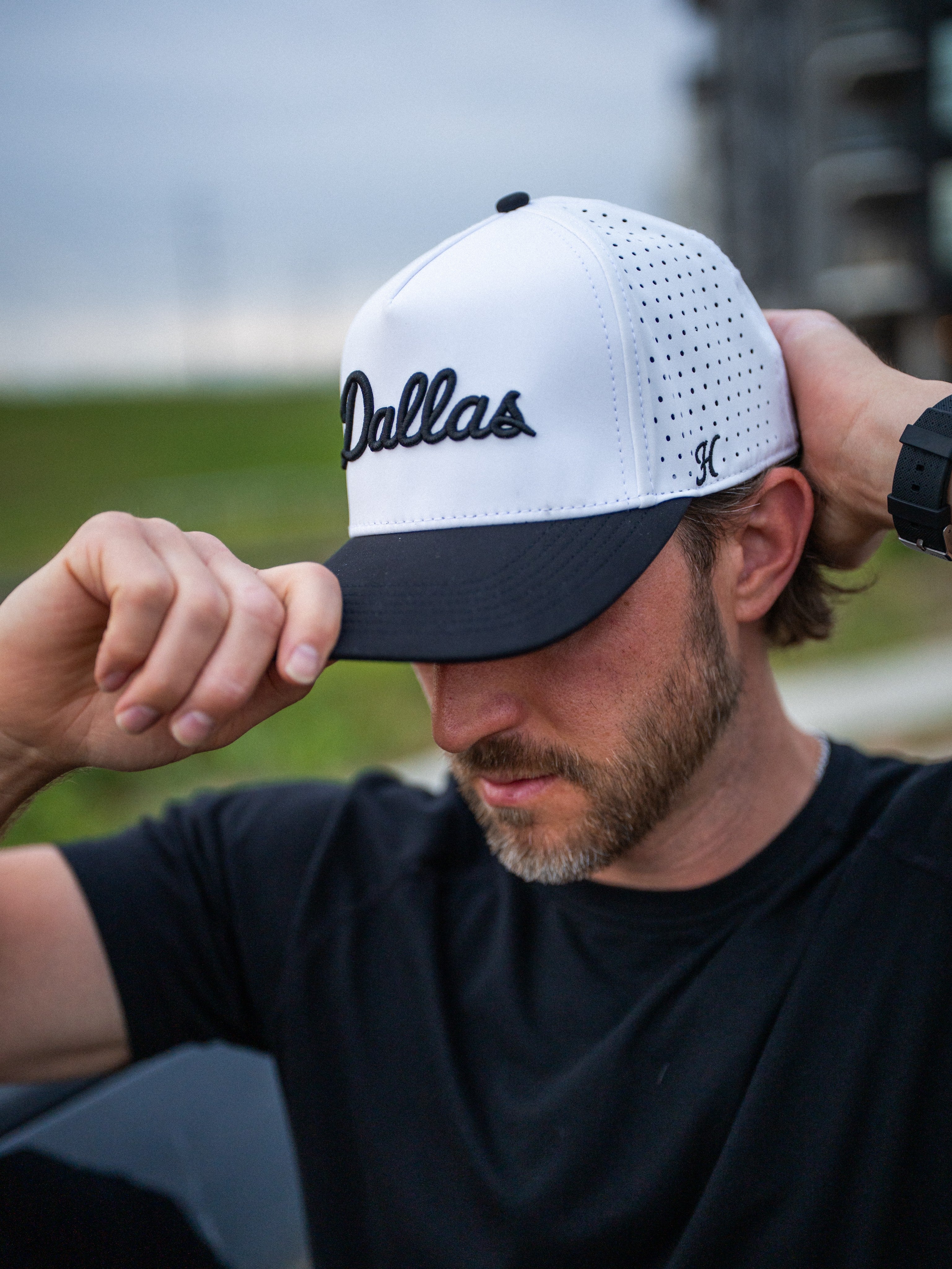 Man wearing a white and black cap with 'Dallas' printed on it, outdoors.