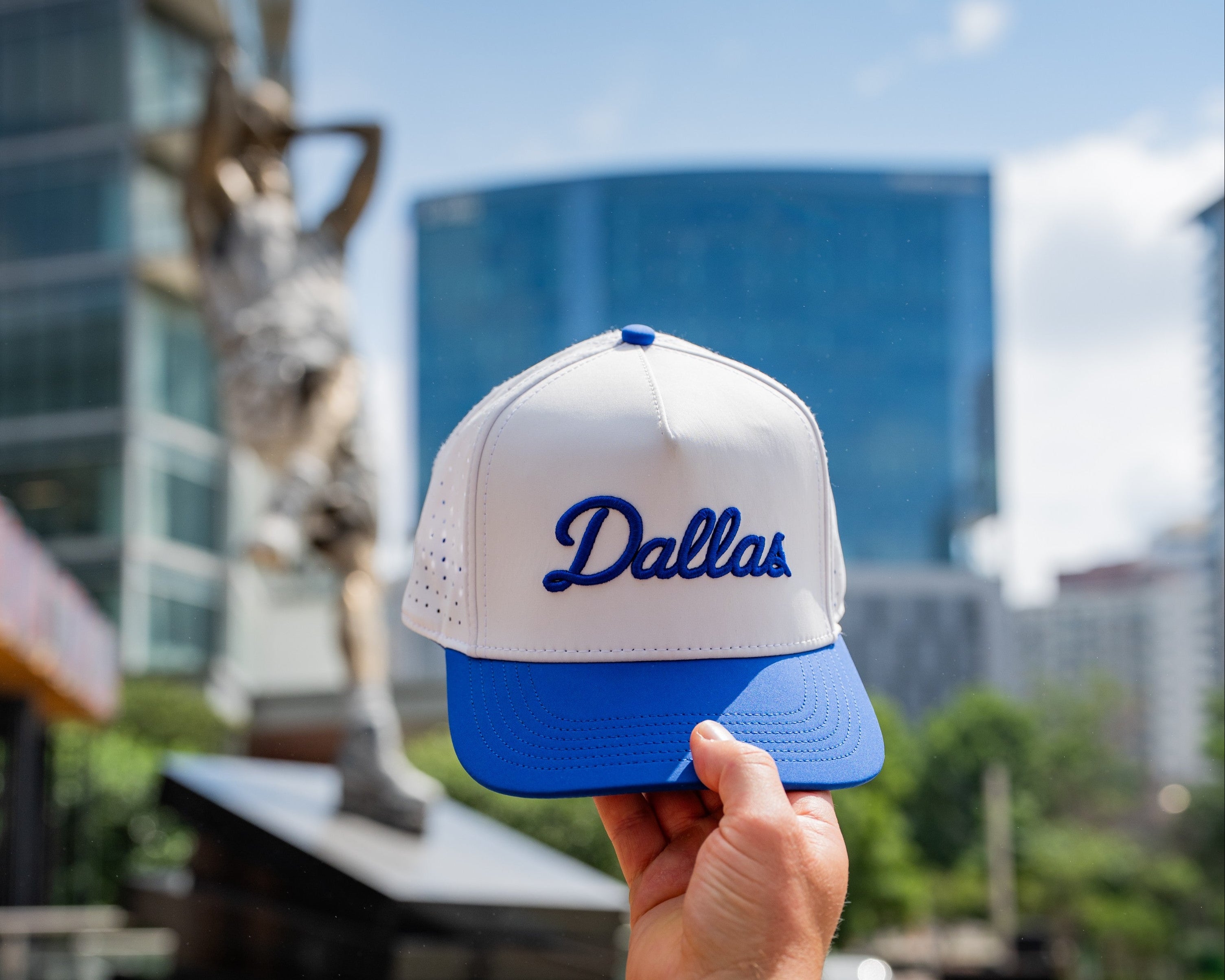 White and blue cap with 'Dallas' text held up against a cityscape background