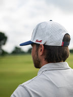 Man wearing a white cap with blue brim and red logo on a blurred green field background