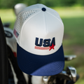 White and blue cap with 'USA' logo on a golf cart in a golf course setting