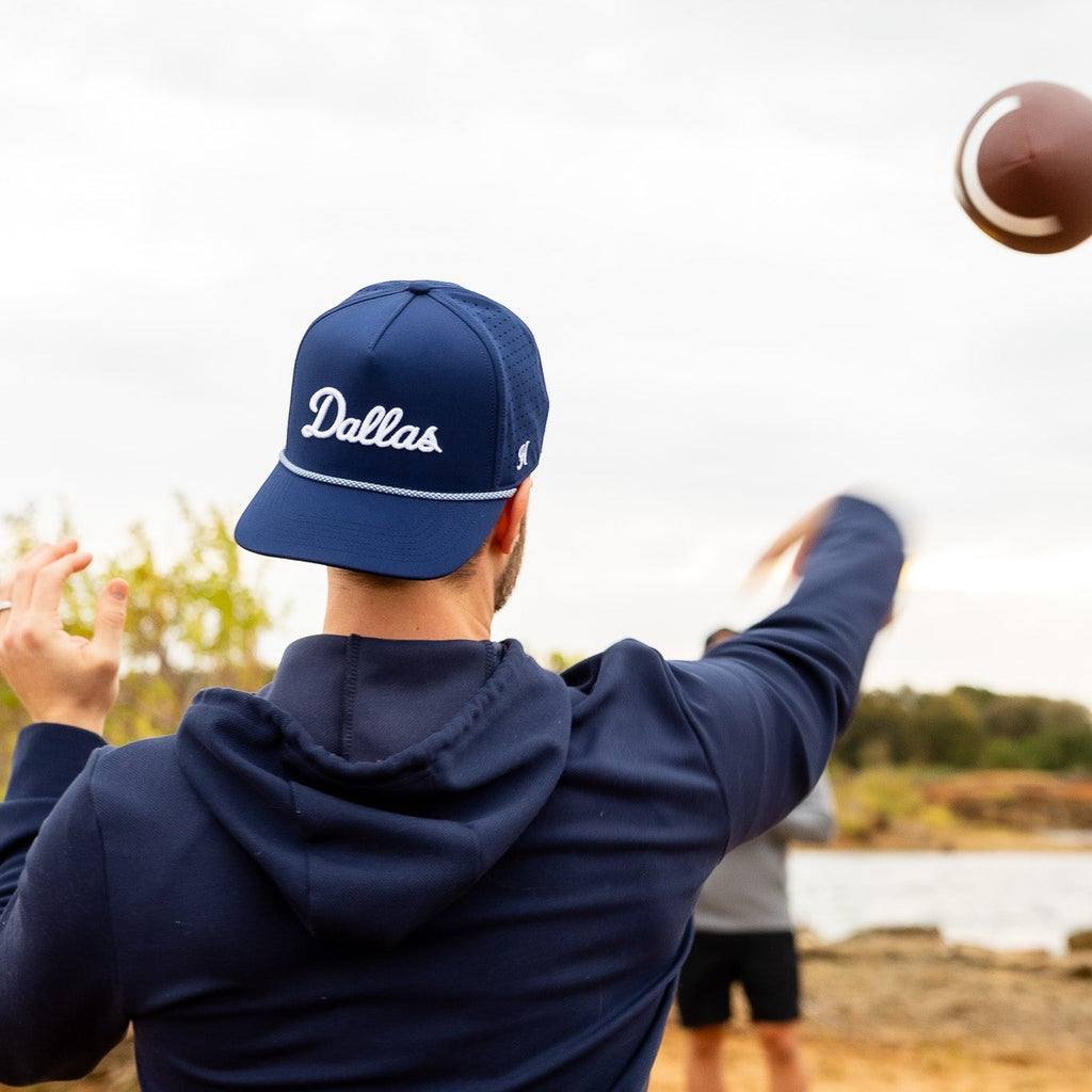 Person wearing a blue 'Dallas' cap and hoodie, outdoors with a football.