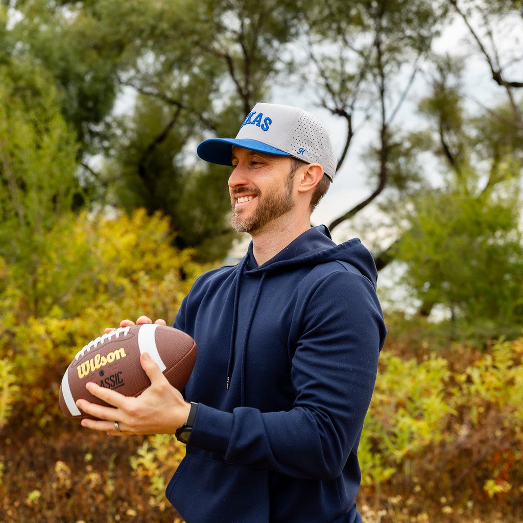 Man holding a football outdoors with trees in the background