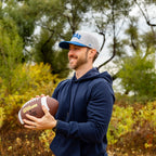 Man holding a football outdoors with trees in the background