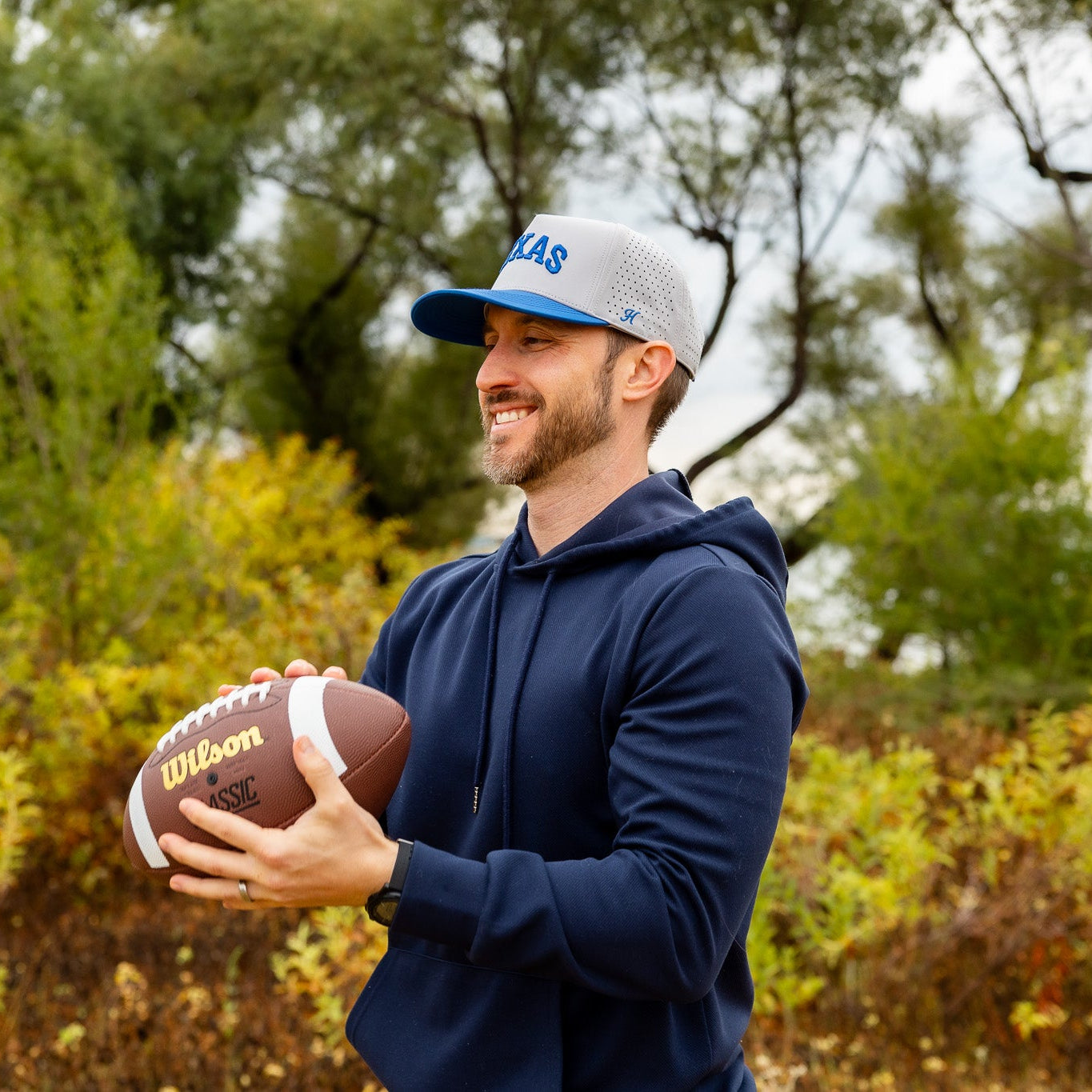 Man holding a football outdoors with trees in the background