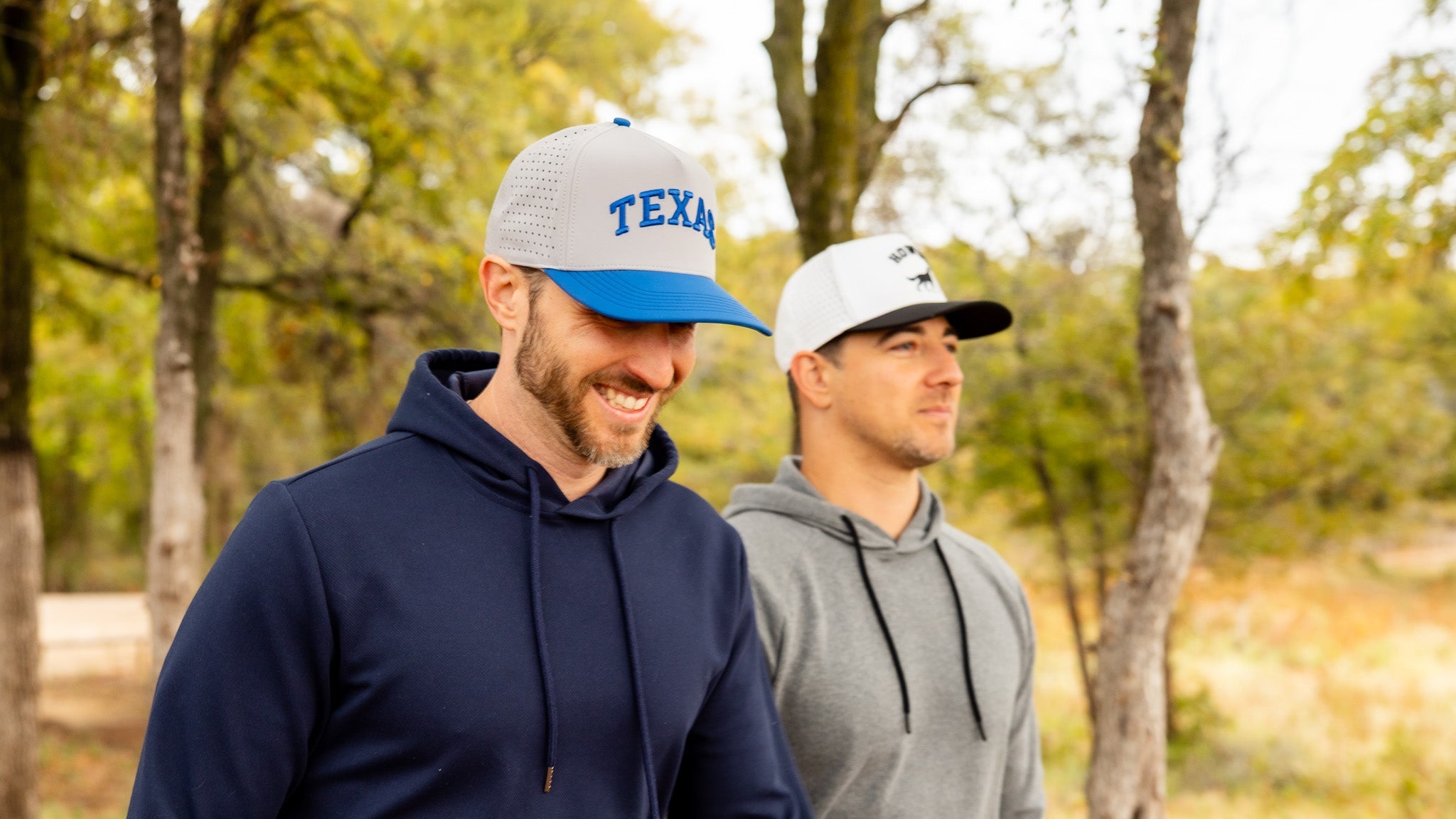 Two men wearing caps with 'Texas' text in a forest setting