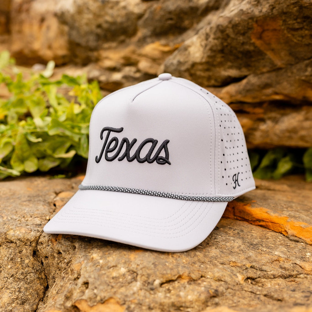 White cap with 'Texas' text on a stone surface with greenery in the background